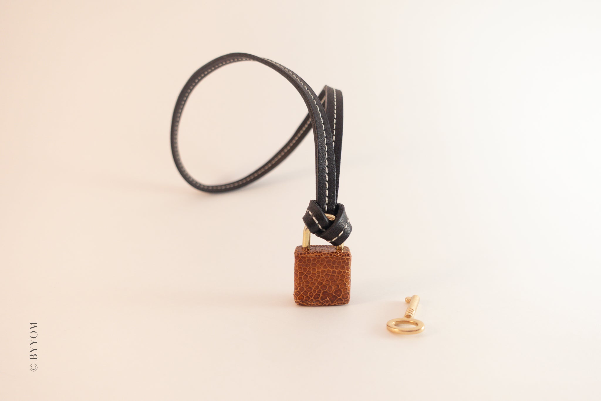 Ostrich leather charm on a black cord with a gold ring on a beige background
