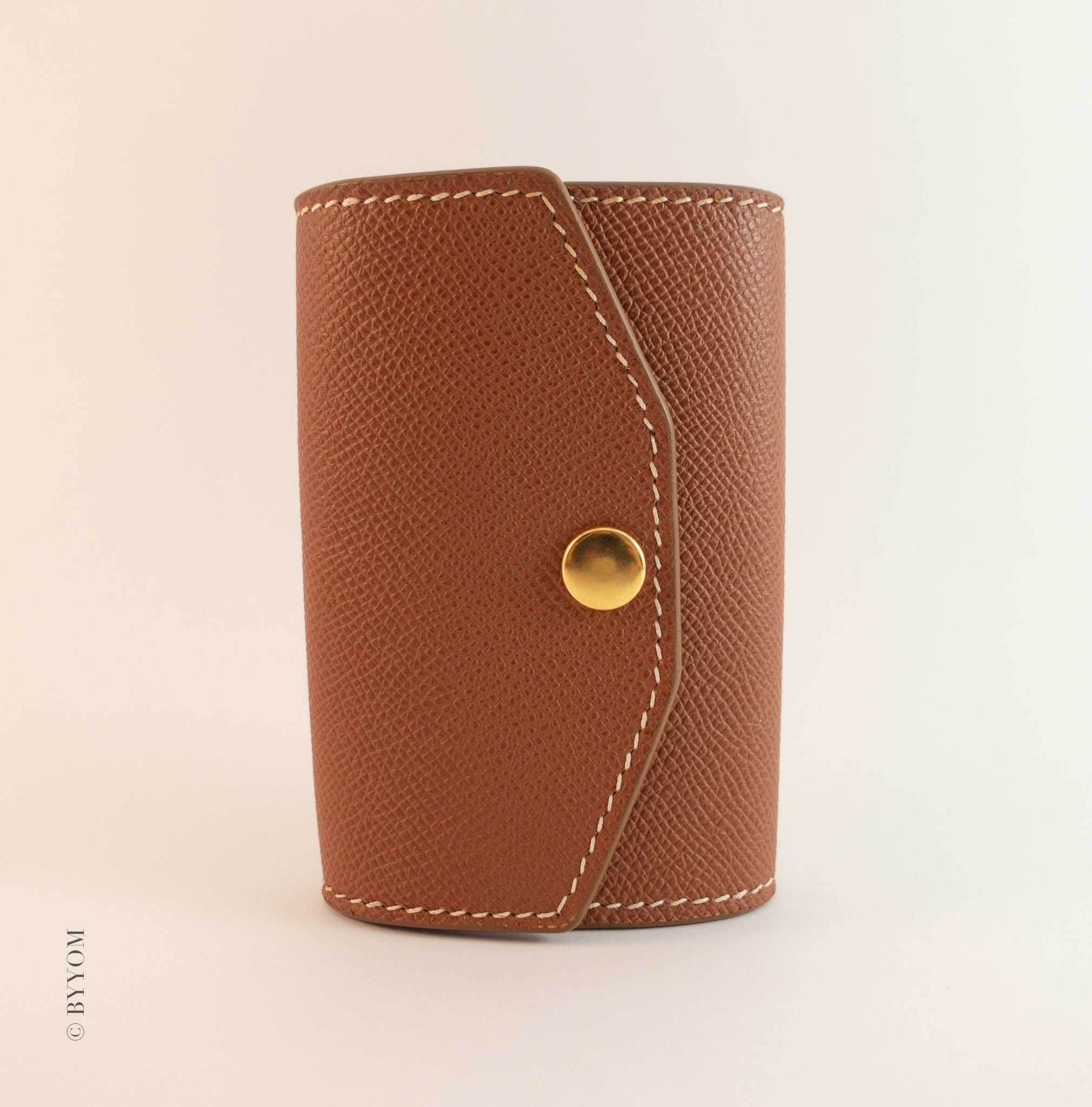 Brown leather key case with a gold button on a beige background