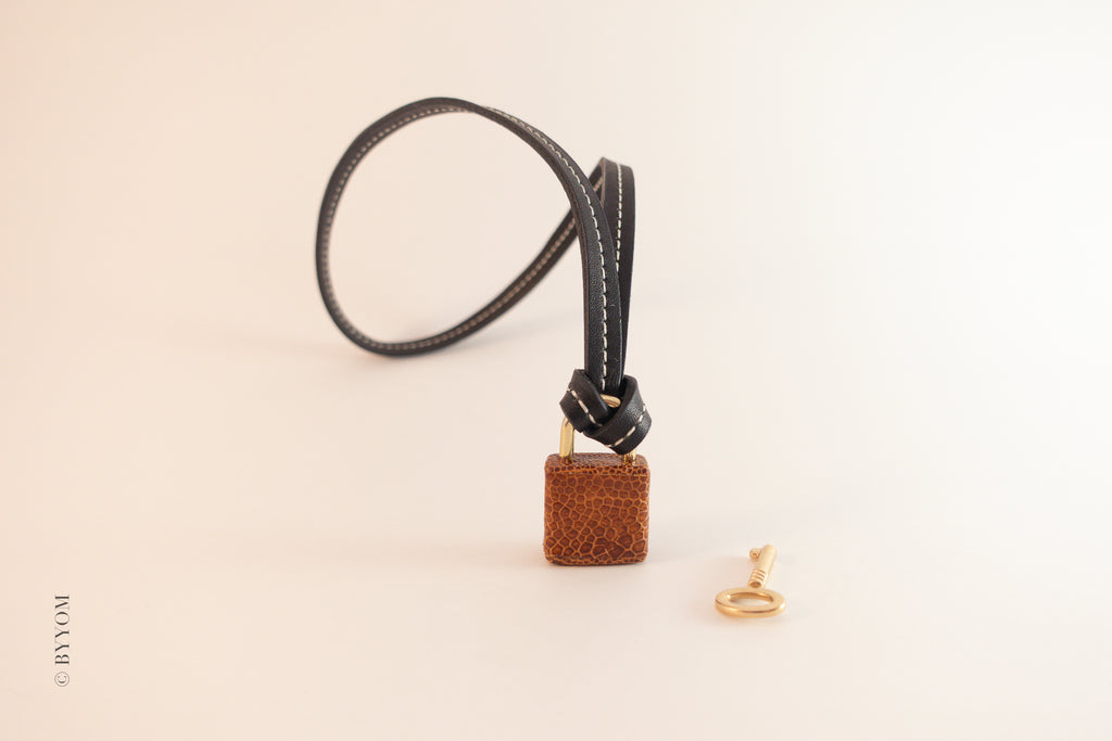 Ostrich leather charm on a black cord with a gold ring on a beige background