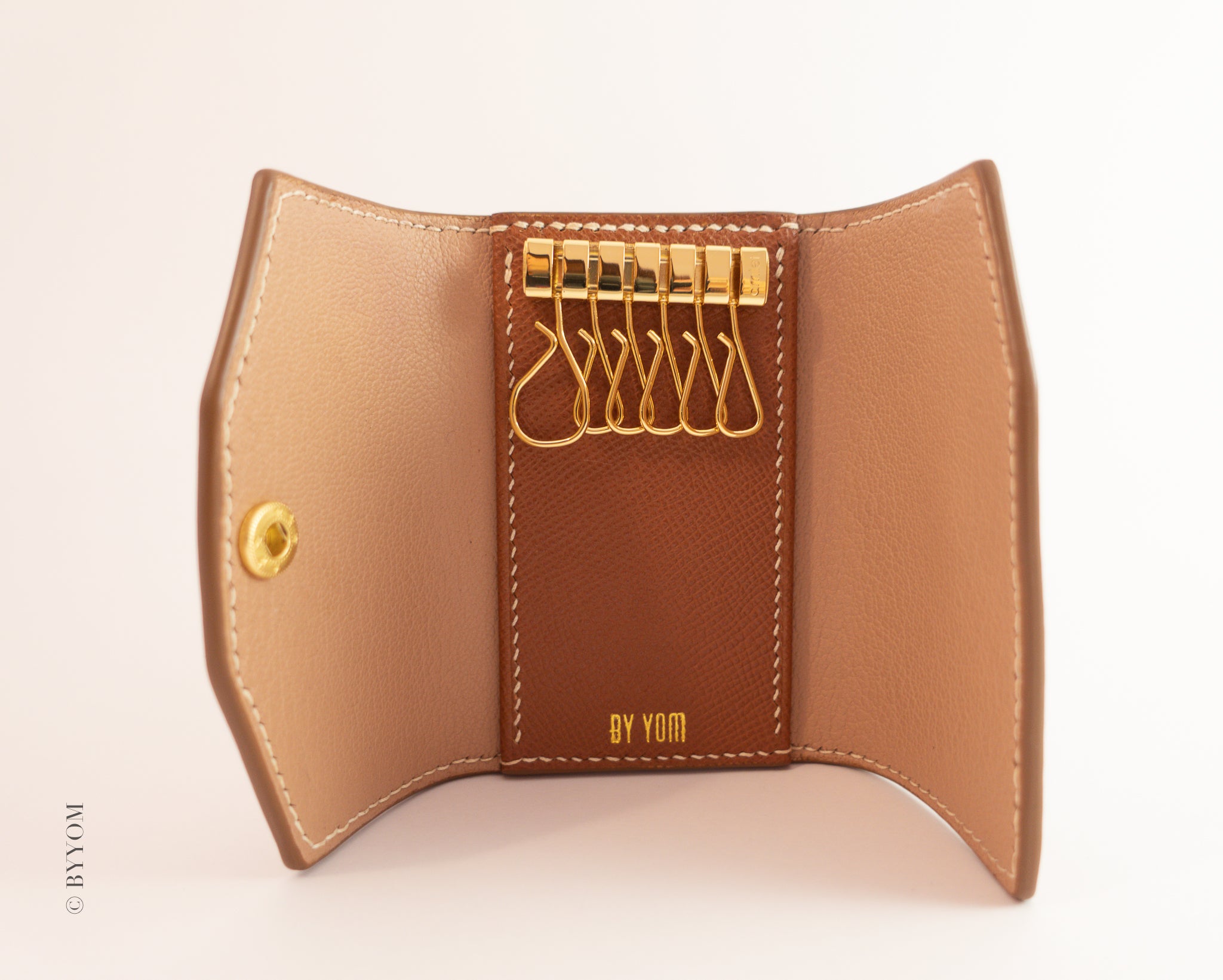 Brown leather key holder with gold accents on a beige background