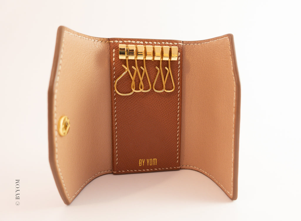 Brown leather key holder with gold keys on a light pink background