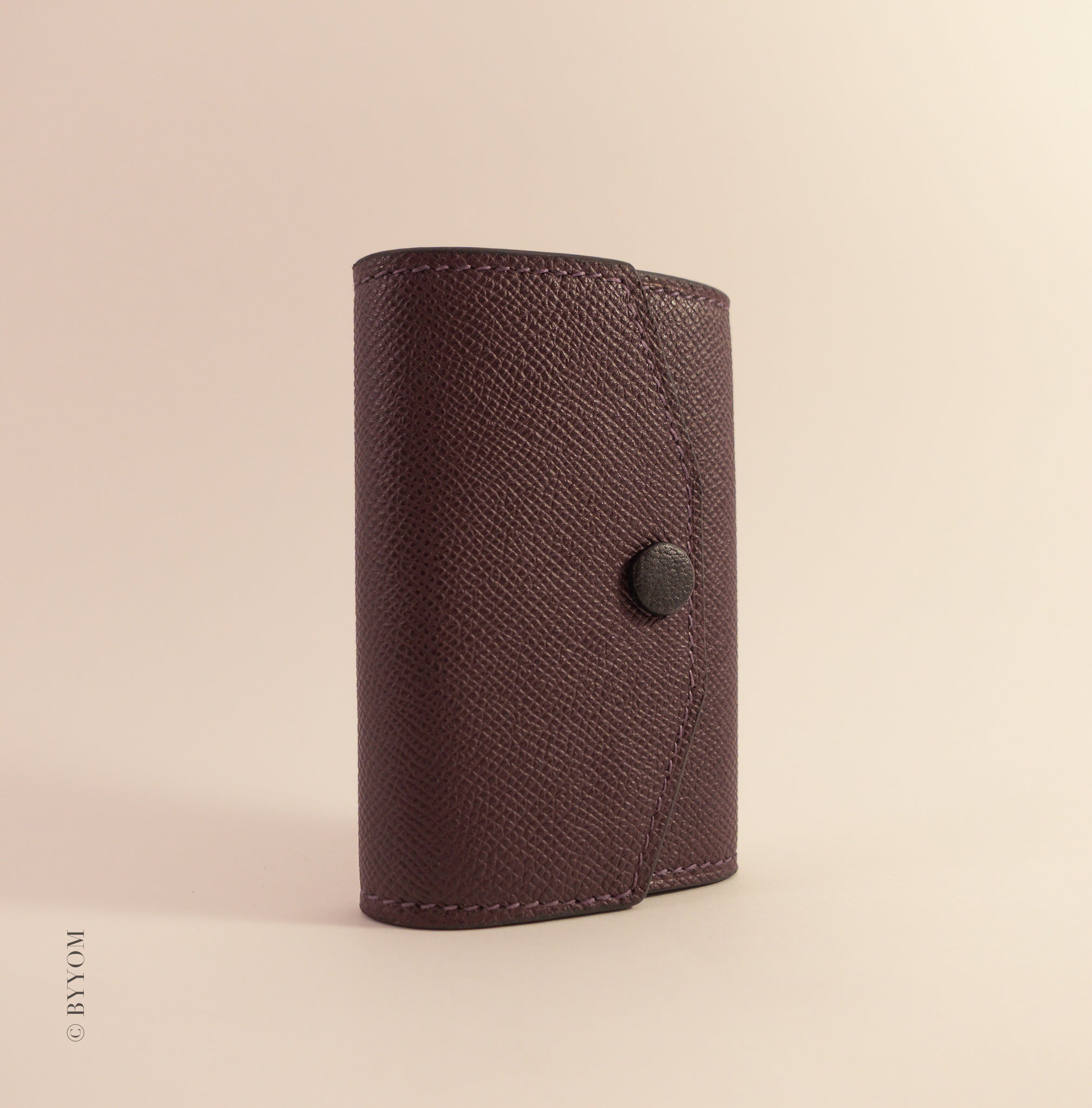 wine color leather wallet with a goat skin covered snap button on a beige background
