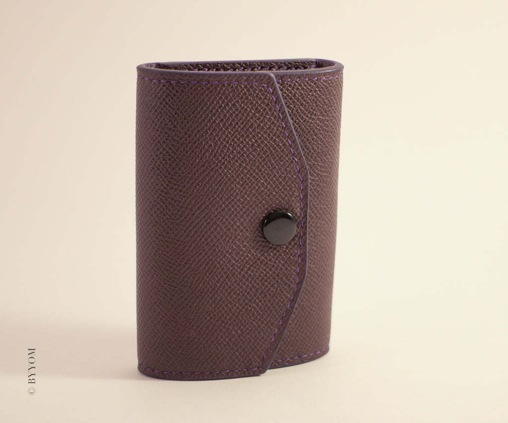 Epsom leather wallet with a shiny black snap button on a beige background
