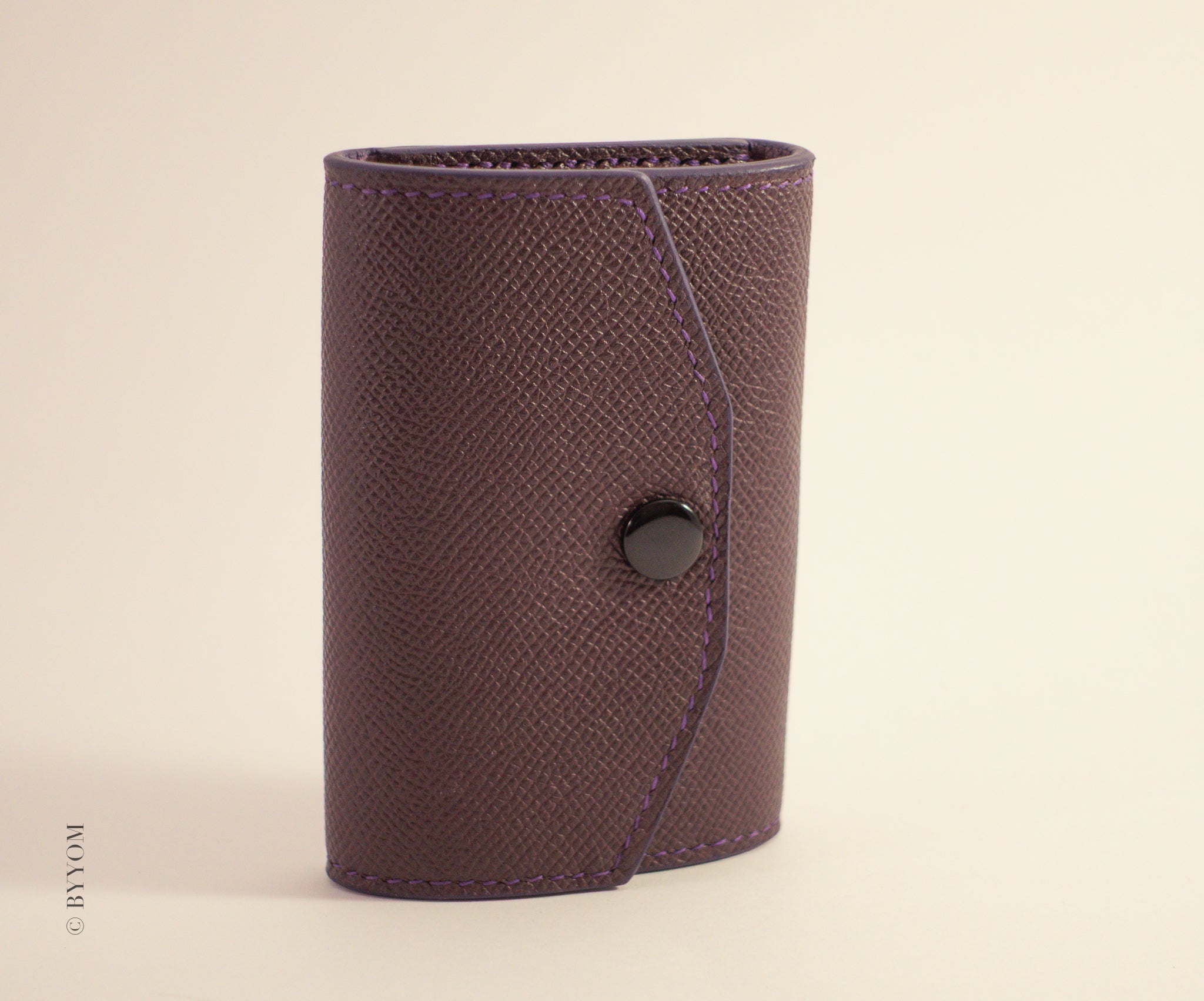 Epsom leather wallet with a shiny black snap button on a beige background