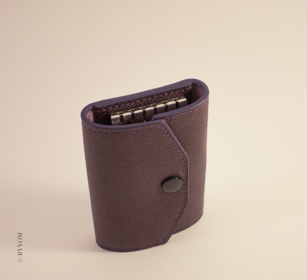 Epsom leather wallet with shiny black snap closure on a beige background