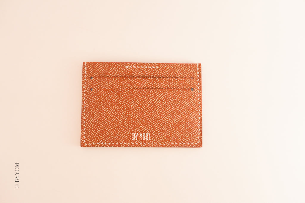 Red textured cardholder with brand BY YOM on a beige background